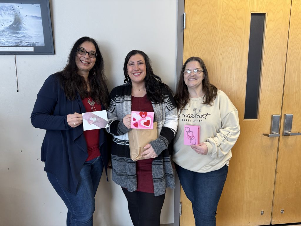 Photo of three women smiling at the camera, holding handmade Valentine's Day cards